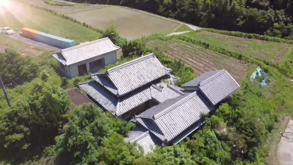 上空から。田んぼと畑に囲まれた中に、入母屋の母屋と別棟が並びます